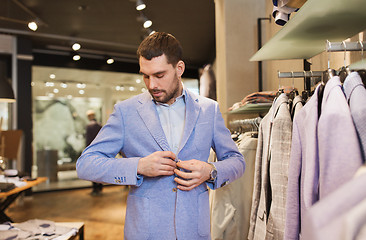 Image showing happy young man trying jacket on in clothing store