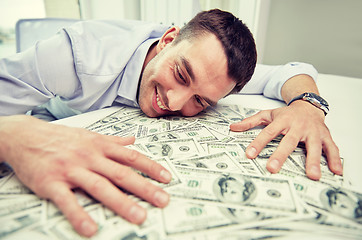 Image showing happy businessman with heap of money in office