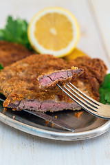 Image showing Piece of beef schnitzel on a fork, lemon and parsley.