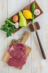 Image showing Raw beef for schnitzel and vegetables on wooden plate. View from