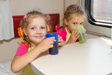 Image showing Two little sisters in a train drinking tea at a table on the lower place in the second-class compartment wagon