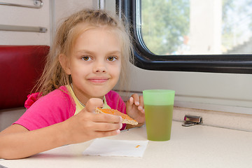 Image showing Six-year girl drinking tea with a sandwich on the train at the table on outboard second-class carriage