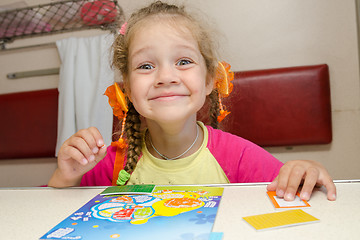 Image showing Little girl on the train with a happy smile sitting at a table on the lower second-class place car and makes the applique