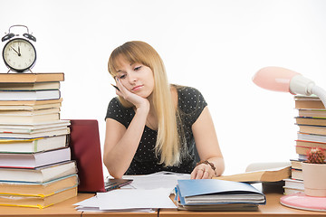 Image showing Student tired of looking at the laptop at the desk in the library crammed with stacks of books