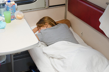 Image showing The girl in a train sleeping on his stomach with his hands behind his head on the lower second-class place car coupe