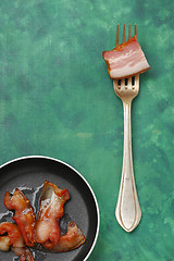 Image showing Fried bacon on a pan and silver fork with raw bacon piece