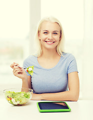 Image showing smiling woman eating salad with tablet pc at home