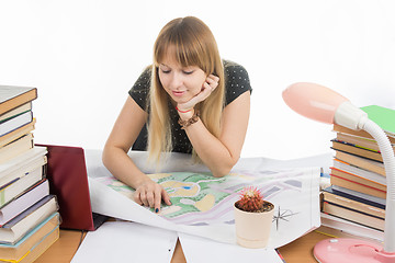 Image showing A girl student with a smile looks at a drawing master plan at a table cluttered with books