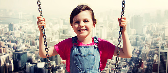 Image showing happy little girl swinging on swing over city
