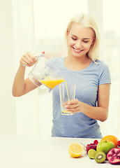 Image showing smiling woman pouring fruit juice to glass at home