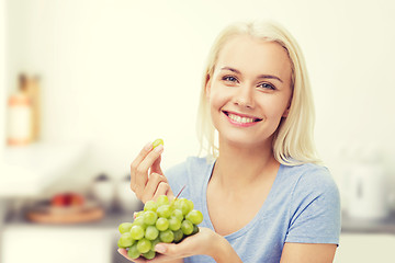 Image showing happy woman eating grapes on kitchen