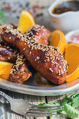 Image showing Fried chicken drumsticks with sesame seeds and orange slices.