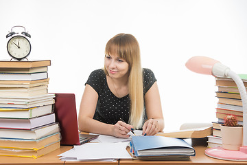 Image showing A student at a table littered with books in the library with a smile looking at the laptop