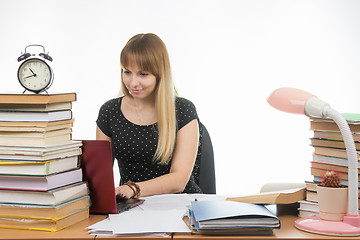 Image showing The girl behind the desk littered with books smiling in a laptop information gathering