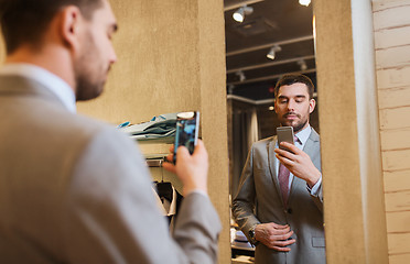 Image showing man in suit taking mirror selfie at clothing store