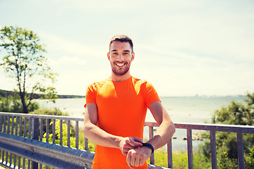 Image showing smiling young man with smart wristwatch at seaside