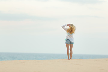 Image showing Woman on sandy beach in white shirt at dusk. 