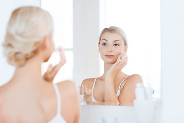 Image showing happy woman applying cream to face at bathroom