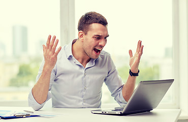 Image showing angry businessman with laptop and papers in office