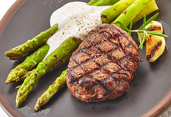 Image showing grilled beef steak and asparagus on dark plate