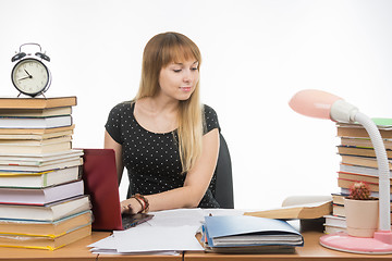 Image showing college student smiling with a laptop in gaining information while sitting at a table littered with books in the library