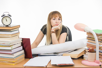 Image showing Girl student sitting sadly at the table crammed with books and papers