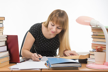 Image showing A student at a table littered with books in the library happily writes synopsis