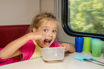 Image showing The girl on the train sits at a table on the lower place in the second-class compartment of the car and eats it with relish spoon