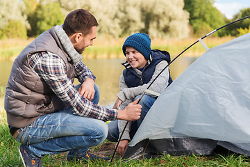 Image showing happy father and son setting up tent outdoors