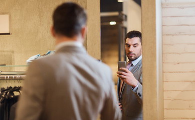 Image showing man in suit taking mirror selfie at clothing store