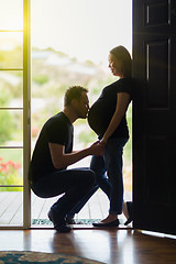 Image showing Husband Kissing Belly of Pregnant Wife In Doorway.