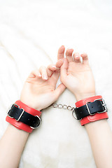 Image showing female hands in leather handcuffs. on the background sheet. sex toys.