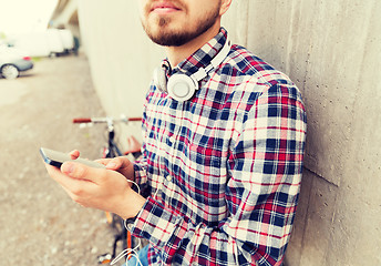 Image showing hipster man in earphones with smartphone and bike