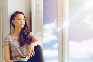 Image showing sad pretty teenage girl sitting on windowsill