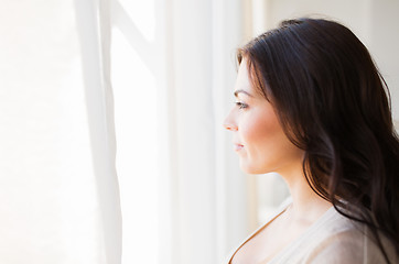 Image showing young woman looking through window at home