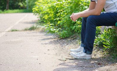 Image showing Young man sitting wearing jeans outdoor.