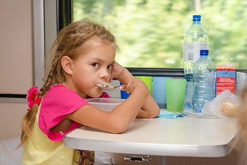 Image showing A six-year girl in a train sitting at the table on the lower place in the second-class compartment of the car and eats porridge spoon
