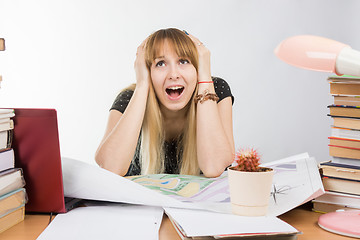 Image showing Girl design student at a desk with a pile of books and projects in desperation grabbed the head