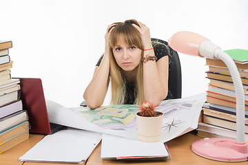 Image showing Student designer behind a desk with a pile of books and projects sits holding his head in his hands