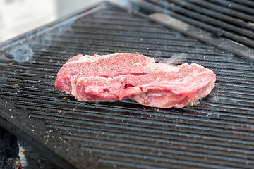 Image showing raw steak with spices on metal grill