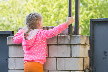 Image showing Five-year girl climbed on a brick fence and looks for him