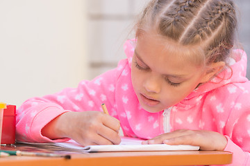 Image showing Schoolgirl is drawing in pencil on the album, in the yard