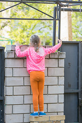 Image showing Five-year girl climbed on a brick fence and looks for him