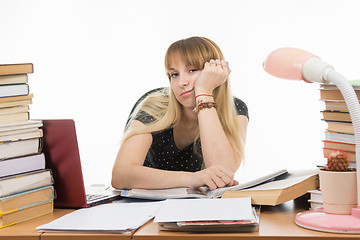 Image showing Student sadly sitting at a table among the stacks of books and papers