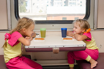 Image showing Two little girls with a happy face looking at each other on the train sitting at the table on outboard second-class carriage