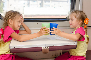 Image showing Two little sisters in identical pajamas drinking tea in the train at the table on outboard second-class carriage