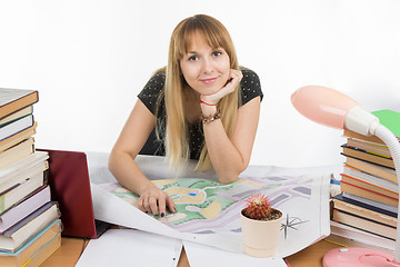 Image showing A girl student at a desk littered with books and drawings with a smile looks in the frame