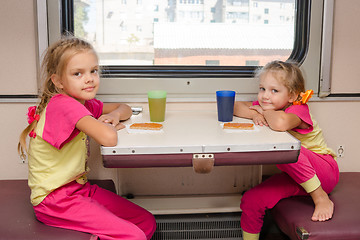 Image showing Two little girls on the train sitting at the table in the outboard second-class car in the same clothes