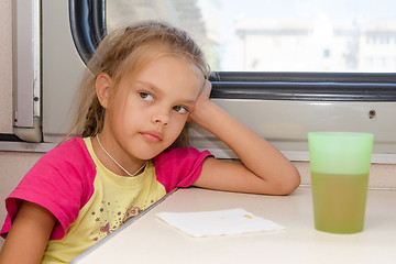 Image showing Six-year girl thoughtfully and tired sitting on the train at the table in the second-class compartment