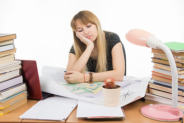 Image showing A girl student at a table with a pile of books, drawings and projects sitting sadly leaning on hand and eyes closed